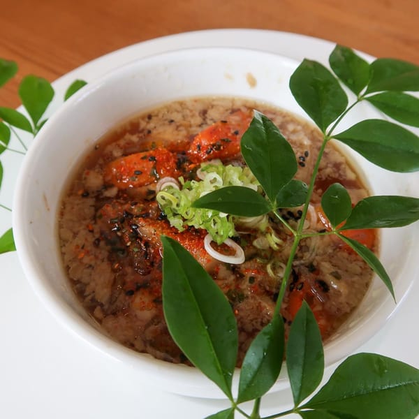 Japanese soup with red ingredients, green onions, and spices, garnished with fresh green leaves.