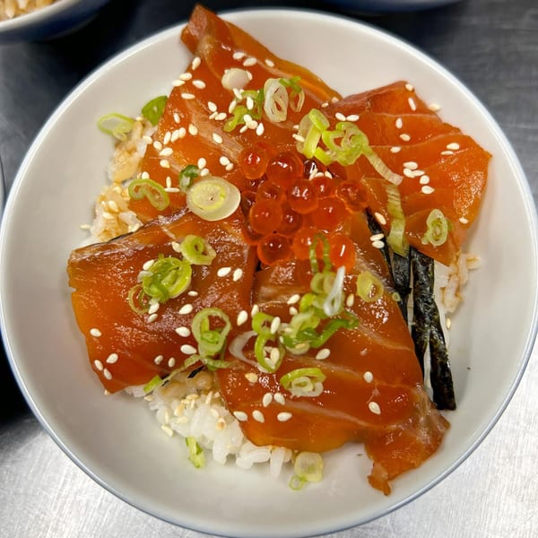 A white bowl of Ko Japanese Dining's salmon donburi with salmon sashimi, roe, green onions, and sesame seeds.