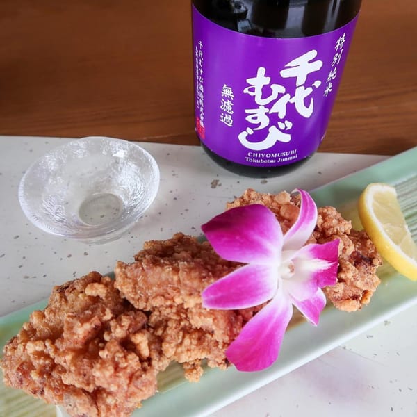 Crispy fried chicken karaage with a purple orchid, lemon wedge, sake cup, and sake bottle.