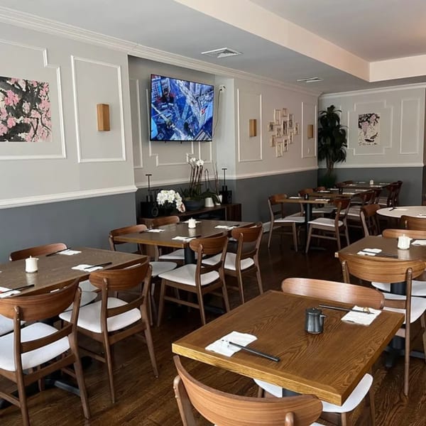 Interior of Ko Japanese Dining with wooden tables, chairs, and a TV on a light gray and dark gray wall.