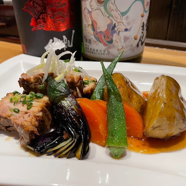 Braised pork belly with eggplant, okra, carrots, and potatoes, served with two sake bottles.